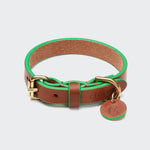 CLOUD7_ Das Hundehalsband Prince Park Cognac/Green hat ein braunes Halsband mit grünen Rändern, eine goldene Schnalle und ein rundes Lederschild an einem goldenen Ring. Es ist aus vegetabil gegerbtem Leder gefertigt und auf der Innenseite für mehr Komfort mit Wildleder überzogen.