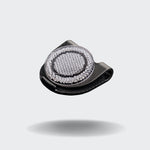 CLOUD7_ Der Orbiloc® Reflective Clip, ein kleines schwarzes Accessoire mit einer strukturierten silbernen Mitte, verbessert die Sichtbarkeit im Dunkeln und ist auf einem schlichten hellgrauen Hintergrund mit einem weichen Schatten darunter abgebildet.