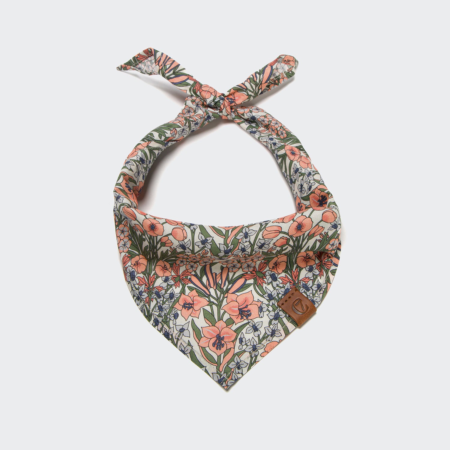 CLOUD7_ Das Hundehalstuch Bandana LTTL Blossoms ist ein dreieckiges Halstuch für Haustiere mit einem Krawattenknoten, einem Blumenmuster in Rosa, Orange und Grün und einem braunen Lederaufnäher. Ein unverzichtbares Hund-Accessoire für stilvolle Welpen. Einfarbig weißer Hintergrund.