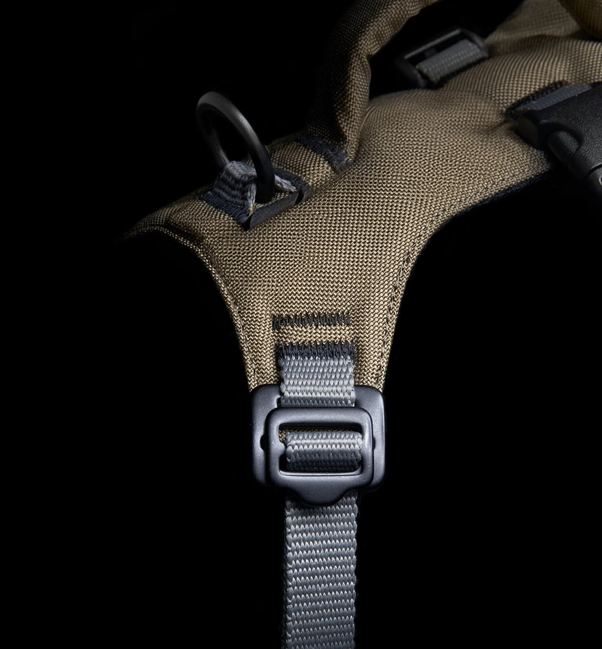CLOUD7_ Eine Nahaufnahme eines Stoffarmbands in Khaki und Grau mit einem schwarzen Metallring und einer Kunststoffschnalle vor schwarzem Hintergrund.