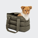 CLOUD7_ Ein kleiner braun-weißer Hund sitzt in einer bauschigen, olivgrünen Tragetasche mit Henkeln vor einem schlichten, hellen Hintergrund.