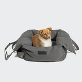 CLOUD7_ Ein kleiner braun-weißer Hund sitzt bequem in der Hundeautositz Getaway Light Graphite Tragbar mit wasserdichtem Outdoor-Gewebe, Memory Foam-Kissen, erhöhten Seiten und Griffen vor einem schlichten hellen Hintergrund.
