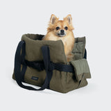 CLOUD7_ Ein kleiner, flauschiger hellbrauner Hund sitzt bequem in der Hundetasche Turin Canvas Olive mit schwarzen Trägern vor einem schlichten hellen Hintergrund.