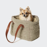 CLOUD7_ Ein kleiner flauschiger Hund sitzt in der Hundetasche Verona Wool Beige - einer weichen, strukturierten beigen Tasche mit braunen Ledergriffen - und blickt nach vorne auf einen schlichten weißen Hintergrund.
