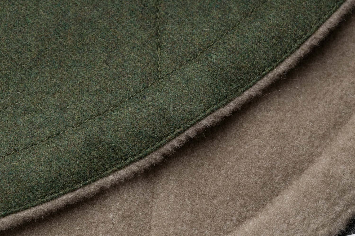 CLOUD7_ Nahaufnahme der Kanten zweier Wollstoffstücke – eines in Grün und eines in Beige –, die deren Struktur und die Details der Nähte zeigen.