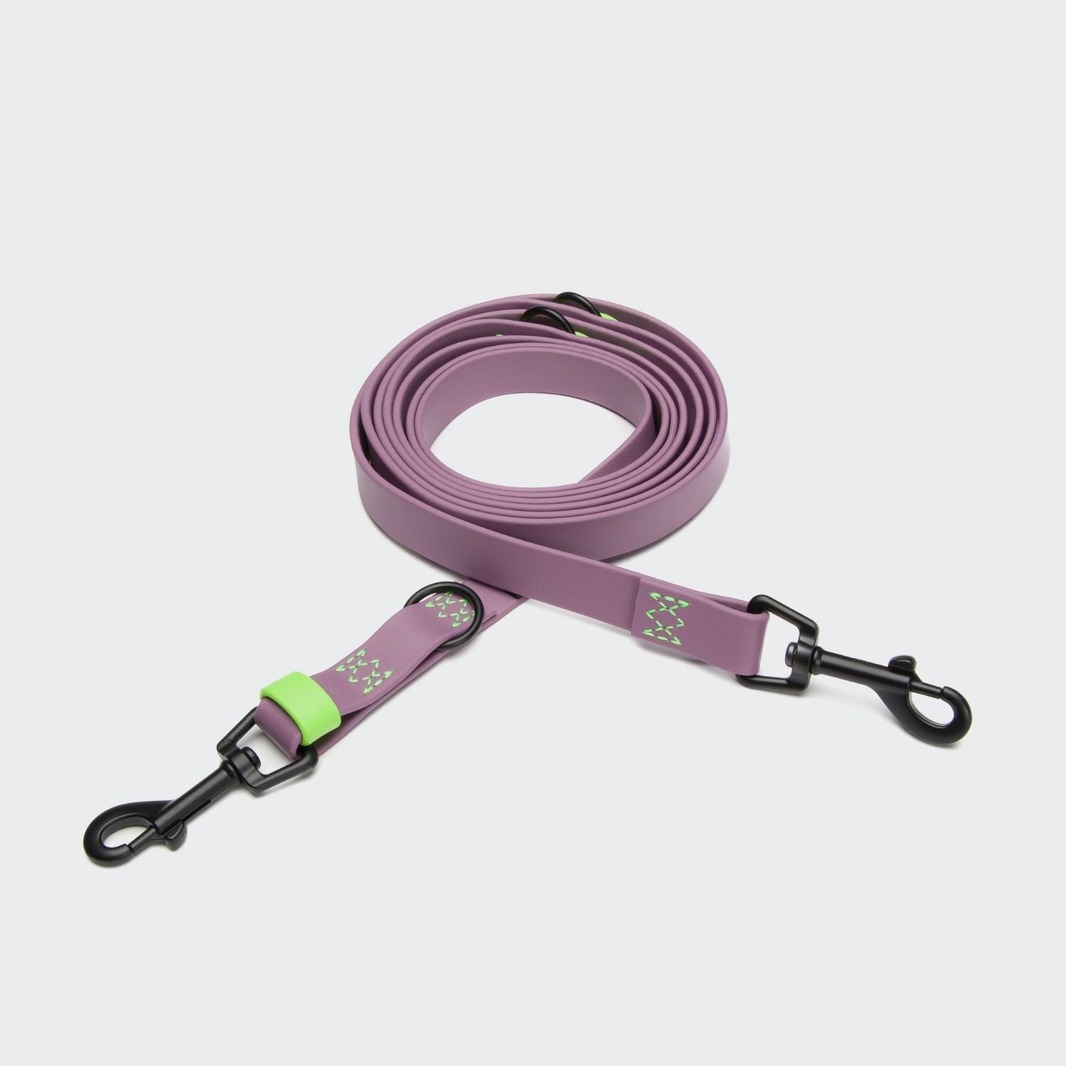 CLOUD7_ Die Hundeleine verstellbar BioThane Ipanema Lilac ist eine aufgerollte lavendelfarbene Leine mit schwarzen Metallverschlüssen an beiden Enden, grünen Akzenten und kleinen dekorativen Mustern in der Nähe eines Verschlusses, dargestellt vor einem schlichten hellen Hintergrund.
