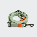 CLOUD7_ Eine Freihandleine aus BioThane „Ipanema Mint-Neon Orange“ aus hellgrünem Material mit schwarzen Metallklammern und leuchtend orangefarbenen Zierstreifen ist ordentlich auf einem schlichten weißen Hintergrund aufgerollt.