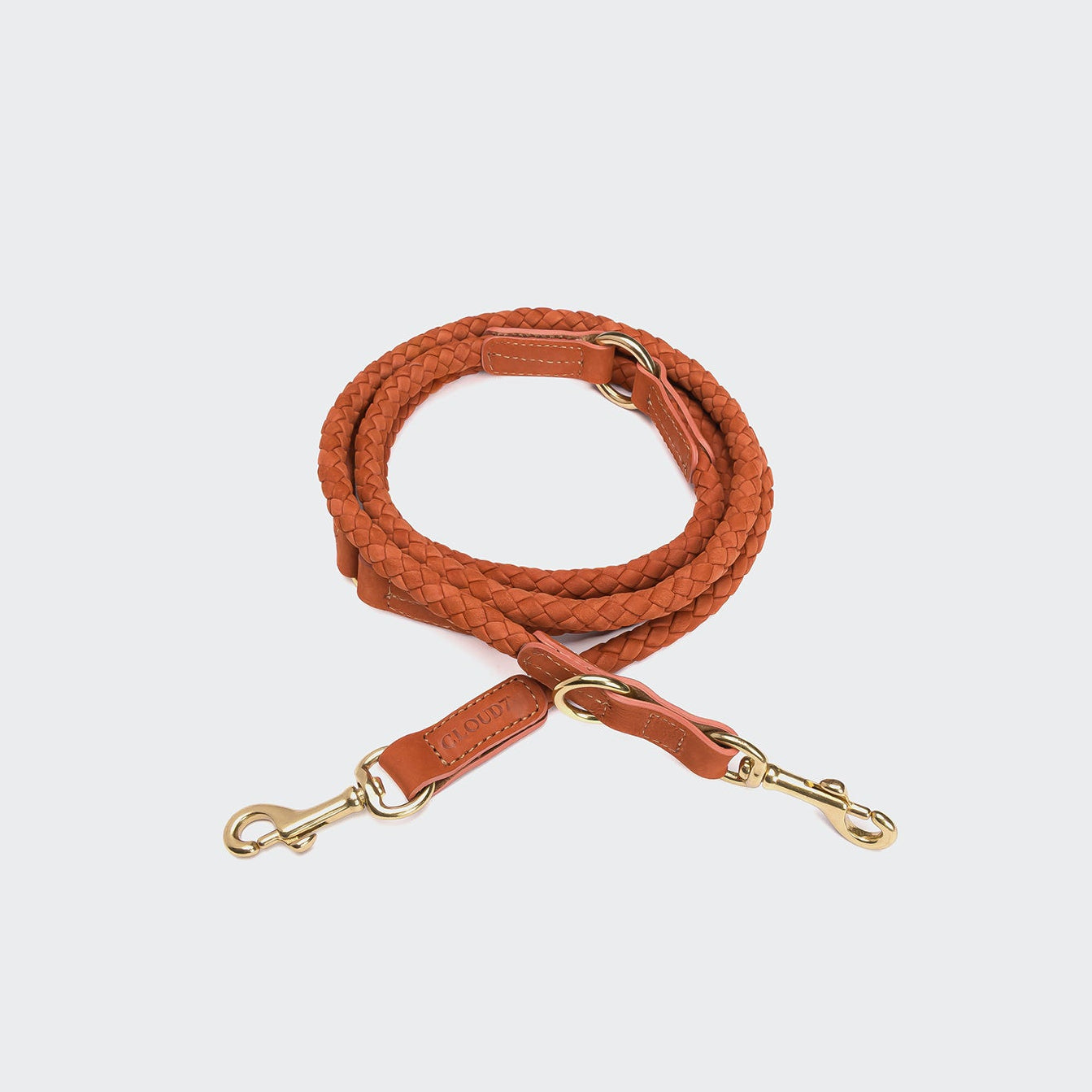 CLOUD7_ Die Hundeleine Ravello Rust ist eine handgefertigte, gewickelte Nubuklederleine in Tan mit goldfarbenen Metallverschlüssen an beiden Enden, präsentiert auf hellgrauem Hintergrund.