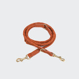 CLOUD7_ Die Hundeleine Ravello Rust ist eine handgefertigte, gewickelte Nubuklederleine in Tan mit goldfarbenen Metallverschlüssen an beiden Enden, präsentiert auf hellgrauem Hintergrund.