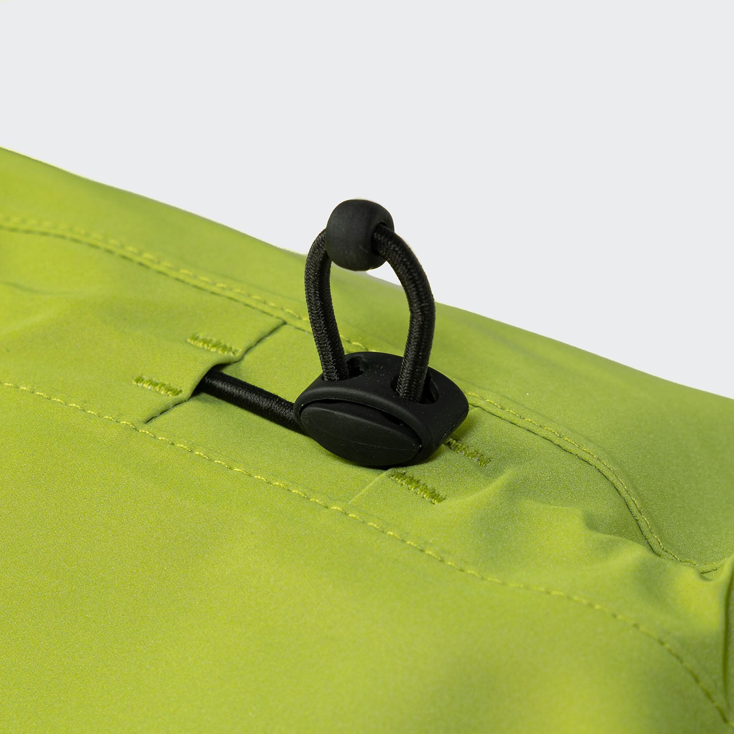 CLOUD7_ Nahaufnahme eines limettengrünen Stoffes mit schwarzem Gummiband und Kordelstopper, vermutlich Teil einer Outdoor-Jacke oder -Tasche, mit sichtbaren Nähten und einer glatten Textur.
