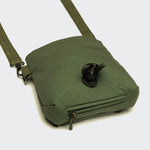 The Leckerlibeutel AKTIV Olive is a small green crossbody bag with a zippered front pocket and a roll of black waste bags partially pulled through its circular front opening. The strap has a subtle pattern—ideal for walks or Hundetraining Tasche.