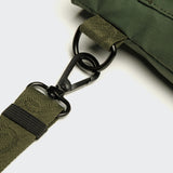 Close-up of an olive green Leckerlibeutel AKTIV Olive strap with a black metal swivel hook attached to a matching green bag, shown on a light gray background.
