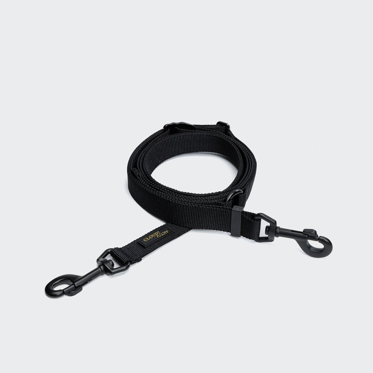 CLOUD7_ Die L-1 Freihandleine AKTIV Black ist eine aufgerollte, verstellbare Hundeleine aus recyceltem Polyester mit Metallhaken an beiden Enden, abgebildet auf einem schlichten hellgrauen Hintergrund.