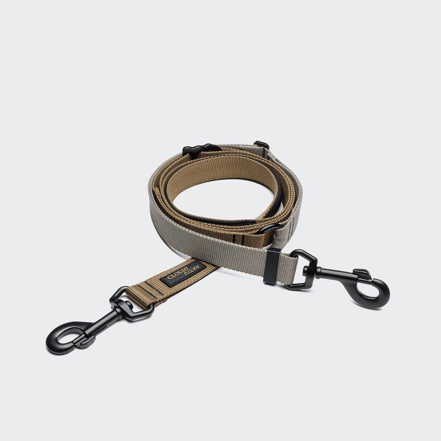 CLOUD7_ Die L-1 Freihandleine AKTIV Khaki/Grau ist eine aufgerollte, zweifarbige, verstellbare Hundeleine in Khaki und Grau aus recyceltem Polyester mit schwarzen Metallverschlüssen an beiden Enden und einem CLIFTON SUPPLY Stoffetikett.