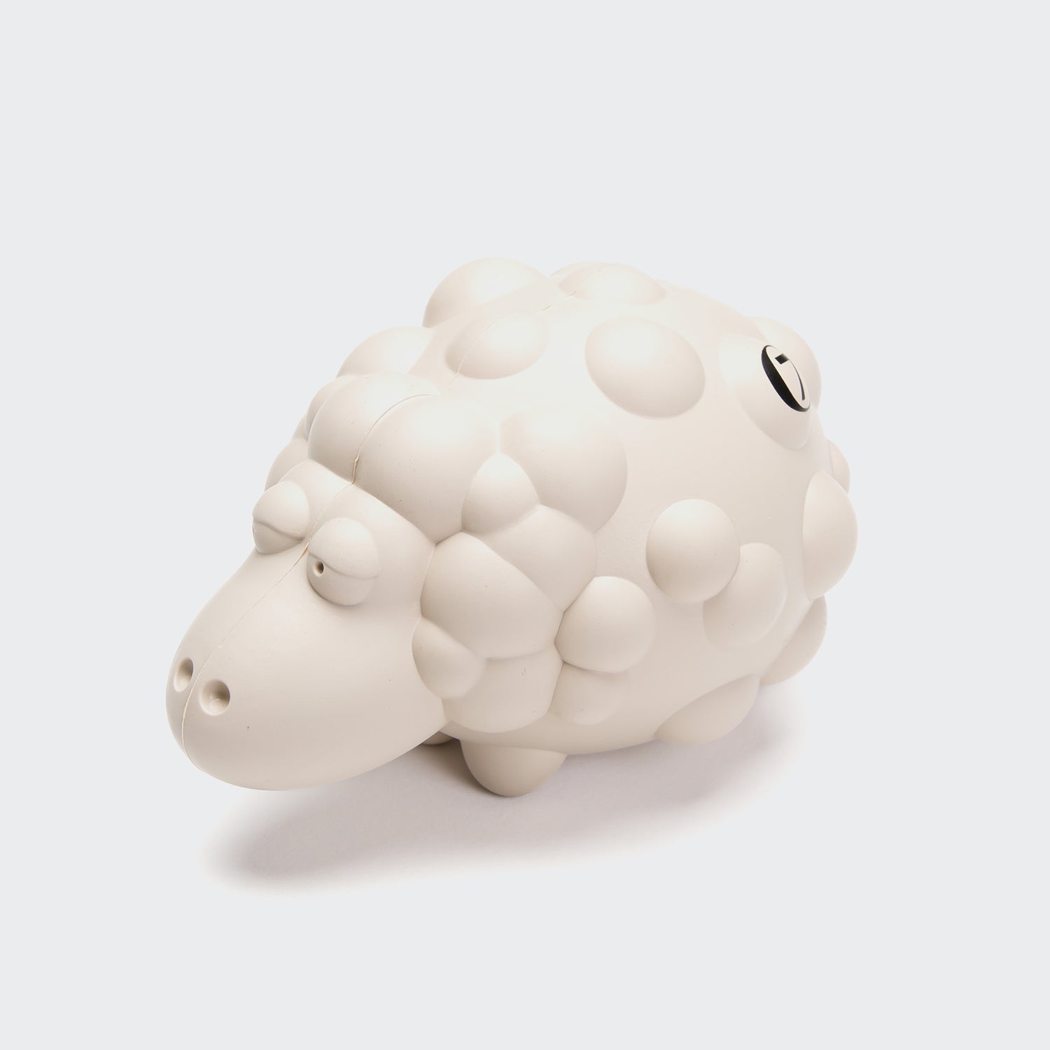 CLOUD7_ Das Kau- & Apportierspielzeug Schaf Meryl Off-White ist ein weißes Hundespielzeug im Cartoon-Stil mit einem holprigen Körper und einem verschlafenen Gesicht, hergestellt aus Naturkautschuk - perfekt als Kau- oder Apportierspielzeug für Hunde. Abgebildet auf einfarbig weißem Hintergrund.