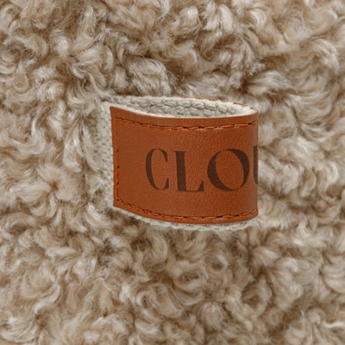 Eine Nahaufnahme eines strukturierten, gewellten, beigen Stoffes mit einem braunen Lederetikett, auf dem teilweise das Wort „CLOU“ in Prägung zu sehen ist.