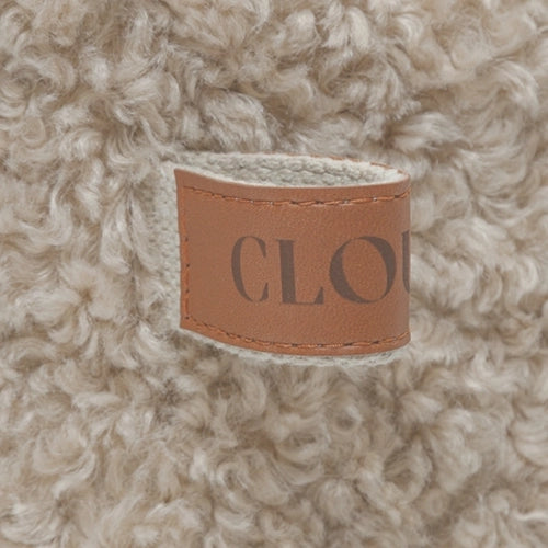CLOUD7_ Eine Nahaufnahme von beigem, lockigem Kunstpelzstoff mit einem braunen Lederetikett, auf dem teilweise das Wort „CLOUD“ in Großbuchstaben zu sehen ist.