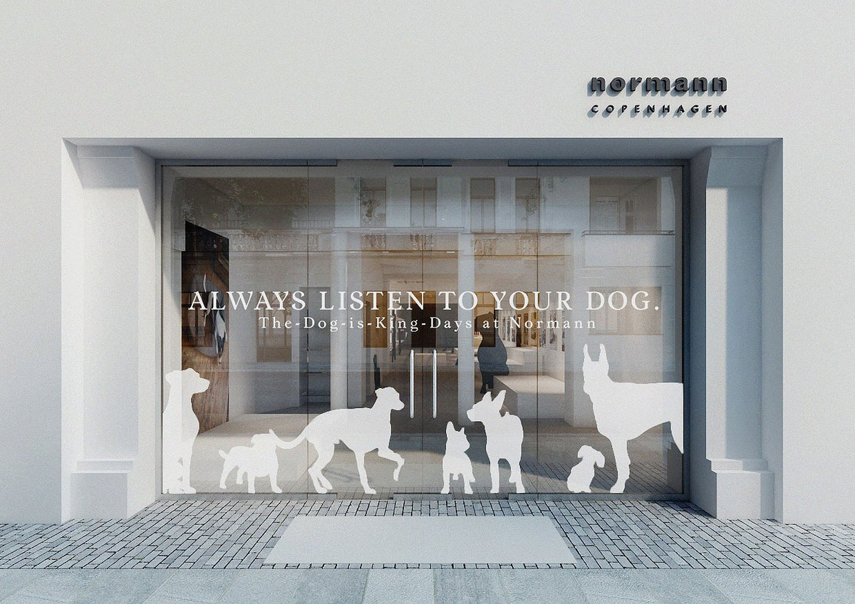 CLOUD7_ Im Schaufenster sind Silhouetten verschiedener Hunderassen zu sehen, begleitet von dem Schriftzug „ALWAYS LISTEN TO YOUR DOG“. Über dem Schaufenster befinden sich die Schilder „The-Dog-is-King-Days at Normann“ und „normann COPENHAGEN“.