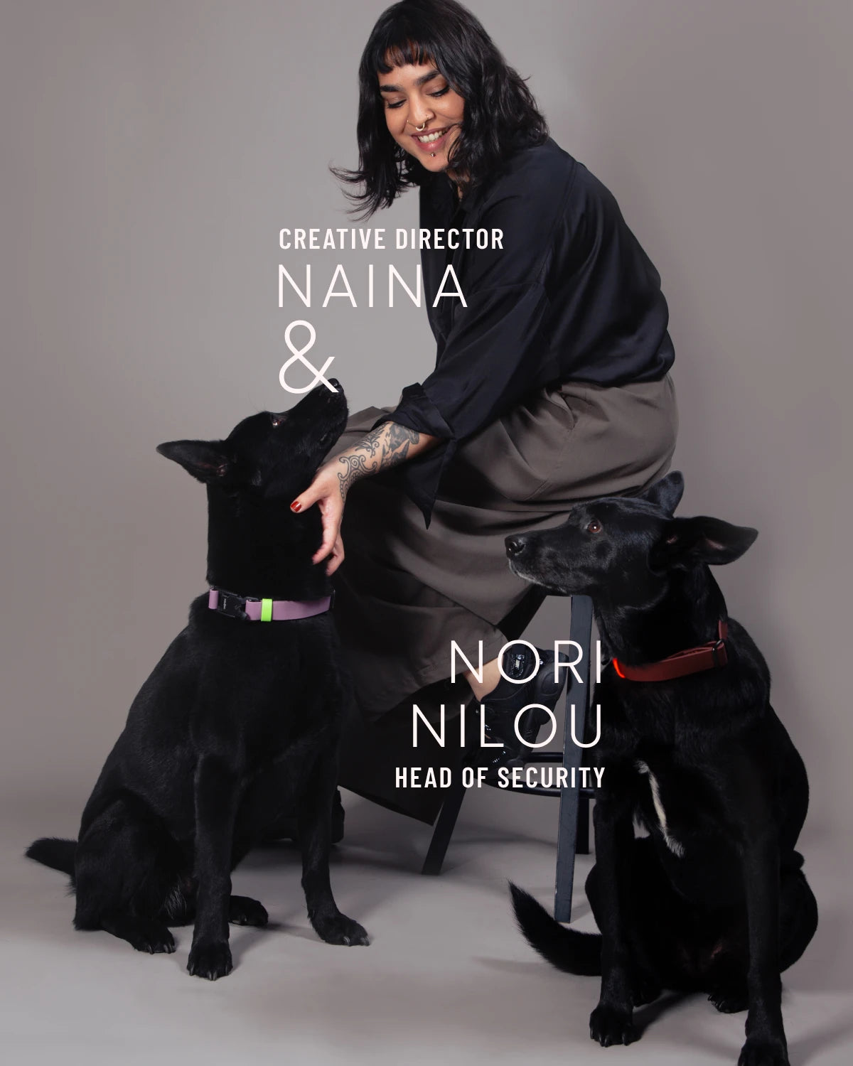 CLOUD7_ Eine Person sitzt auf einem Hocker und lächelt zwei schwarze Hunde an. Der Text auf dem Bild lautet: Kreativdirektorin Naina & Nori, Nilou, Leiterin der Sicherheitsabteilung. Alle drei posieren vor einem einfarbigen Hintergrund.